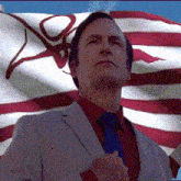 a man in a suit and tie stands in front of a flag