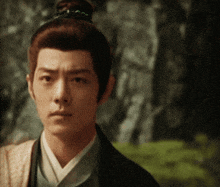 a man with a bun on his head looks at the camera with trees in the background