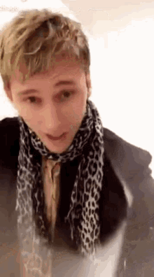 a young man wearing a scarf and a jacket is standing in front of a mirror .