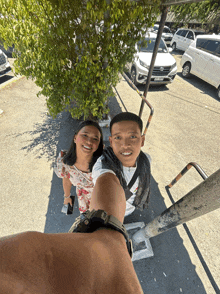 a man and a woman are posing for a picture in a parking lot with cars parked in the background