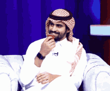 a man wearing a head scarf is sitting on a couch and drinking from a cup