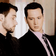 a man in a suit and tie is standing next to another man in a pink shirt