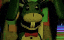 a green and yellow stuffed animal with a bow tie is standing in front of a green wall .