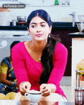 a woman in a pink shirt is sitting at a table with a cup of coffee .