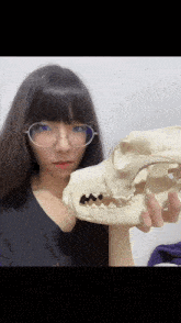 a woman wearing glasses holds a skull in her hand