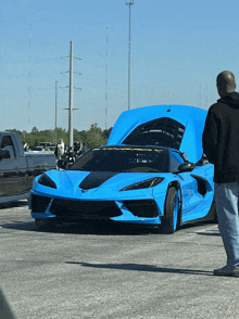 a man stands in front of a blue sports car with its hood up