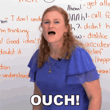 a woman in a blue shirt is standing in front of a white board that says ouch