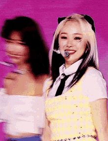 two women are standing next to each other on a stage . one of the women is wearing a yellow top and a tie .