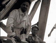 a man in a white coat stands next to another man in a black and white photo