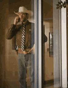 a man wearing a cowboy hat and tie is talking on a cell phone