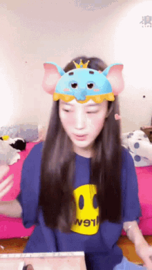 a girl wearing a blue shirt with a yellow smiley face and a blue elephant headband