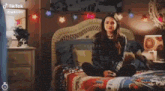 a girl is sitting on a bed in a bedroom with christmas lights .