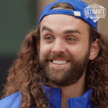 a man with long curly hair and a beard wears a blue hat that says canada 's ultimate challenge