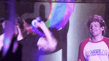 a man in a vans shirt is holding a rainbow balloon while standing next to another man .