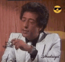 a man in a suit is smoking a cigarette and wearing sunglasses .