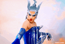 a drag queen in a blue dress is holding a dolphin in her hands