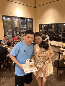 a man in a blue adidas shirt is holding a baby and a cake