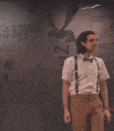a man wearing suspenders and a bow tie stands in front of a wall that says german