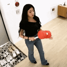 a woman in a black top and blue jeans holds a red object