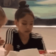 a girl in a black adidas shirt is sitting at a table eating a hamburger .