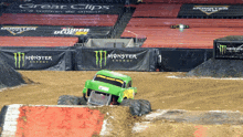 a green monster truck is driving through a dirt track