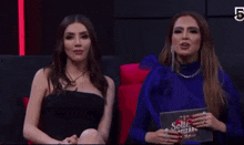 two women are sitting next to each other on a couch and one is holding a sign that says solte criticado .