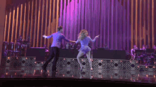 a man and a woman are dancing on a stage in front of purple curtains