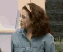 a woman wearing a headband and a denim shirt is making a face .