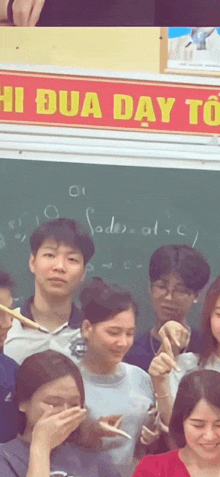 a group of people are standing in front of a blackboard with a sign that says hi dua day toi .