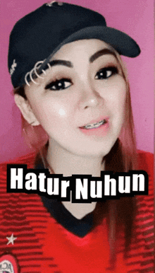 a woman wearing a hat and a red shirt with the words " hatur nuhun " on the bottom