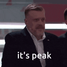 a man in a suit says it 's peak while standing in front of a microphone