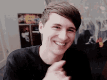 a young man in a black shirt is smiling and pointing at something