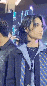a man with long hair is standing next to another man in a jacket and tie .