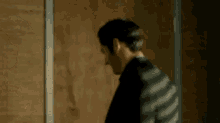 a man in a black suit is standing in front of a wooden door .