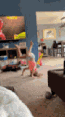 a little girl is doing a handstand in a living room in front of a television .
