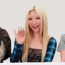a blonde woman wearing a blue plaid shirt is waving her hand