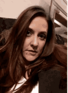 a woman with long brown hair is sitting on a couch taking a selfie .