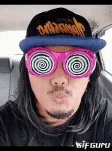 a man wearing hypnotic glasses and a hat with the word dope on it is sitting in a car