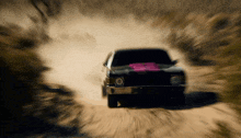 a car is driving down a dirt road with a pink sticker on the windshield
