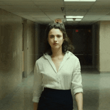a woman in a white shirt is walking down a hallway with an exit sign above her
