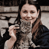 a woman is smiling while holding a cat in her lap