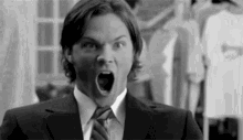 a man in a suit and tie is making a funny face with his mouth open .