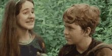 a boy and a girl are standing next to each other in the woods .
