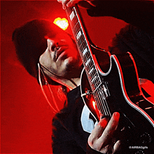 a man playing a guitar in a dark room with a red light behind him