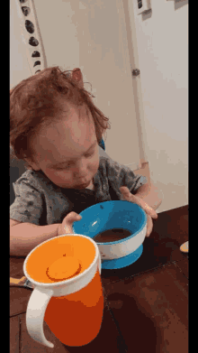 a toddler is sitting at a table with a blue bowl and an orange cup