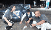 a group of people are squatting in front of a car at a gas station .
