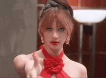 a woman in a red dress with a red flower around her neck is giving a thumbs up