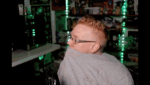 a man wearing glasses and a gray shirt is sitting in front of a computer desk .