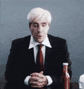 a man in a suit and tie is sitting at a table with his hands folded .