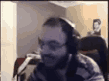 a man with a beard and glasses is wearing headphones and looking at the camera .